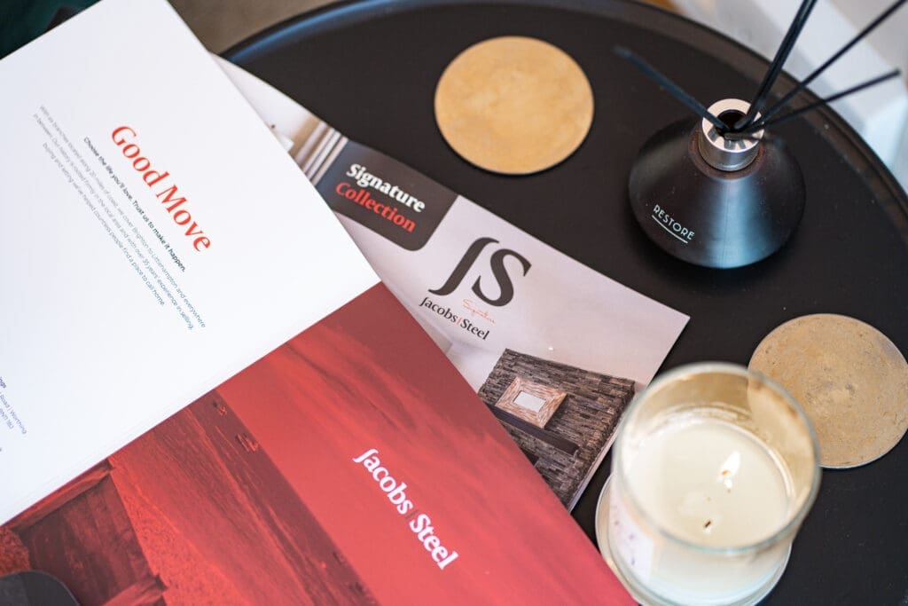 Jacobs Steel brochures laid out open on a coffee table with bamboo coasters, a diffuser and a candle